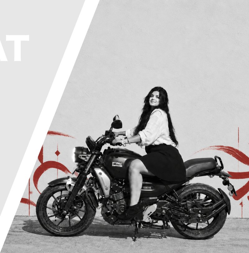 Akanksha on her motorcycle in front of a wall with red brush strokes